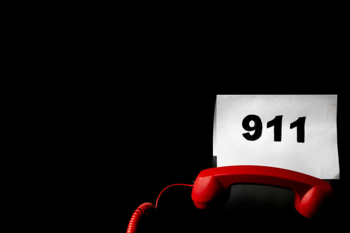 A red telephone next to a sign displaying the number 911 on a dark background