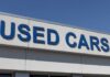 Used-Car Prices Back In the News Sign displaying 'USED CARS' on a dealership building