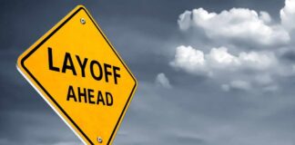 Yellow warning sign indicating layoffs ahead against a cloudy background