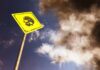 Yellow warning sign with skull symbol under dramatic cloudy sky