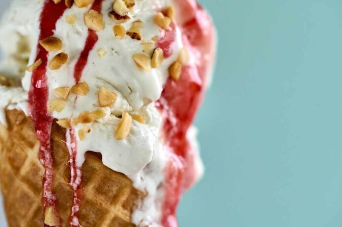 A,Close,Up,Of,A,Waffle,Cone,Filled,With,Homemade Close-up of an ice cream cone topped with strawberry sauce and chopped nuts