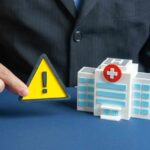 Outrage: Treatment Center TORCHED! A business professional holding a warning sign next to a model of a hospital