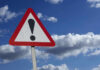 Warning sign with exclamation mark against sky