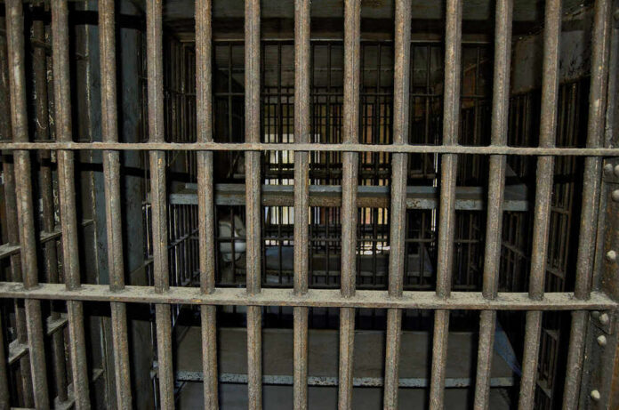 Empty, rusty barred jail cell with metal bunks.