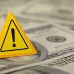 A yellow warning sign placed on a pile of dollar bills