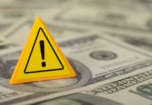 Energy Shock JOLTS Inflation A yellow warning sign placed on a pile of dollar bills