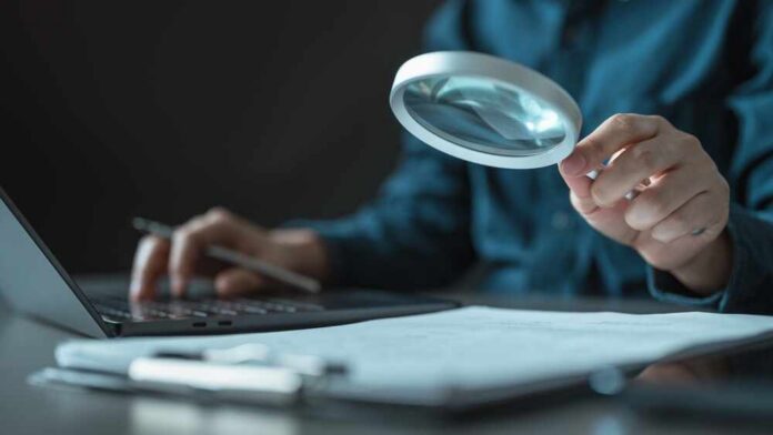 Person using a magnifying glass while working on a laptop