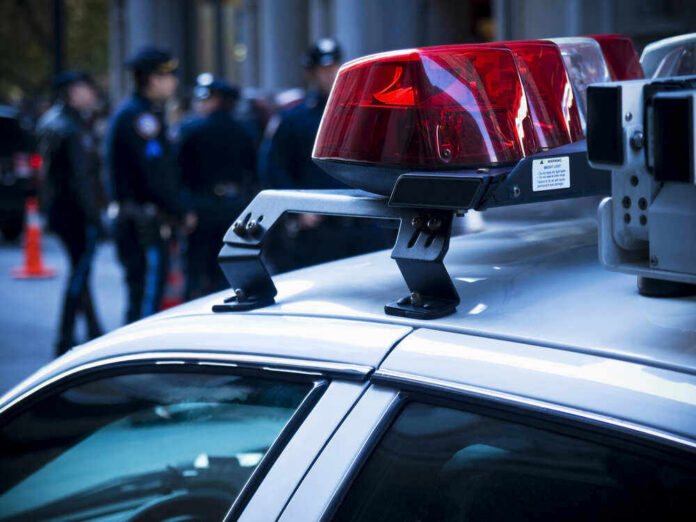 shutterstock_46269745-1 Police car roof with lights, officers in background.
