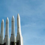 Four white missile launchers pointing upward against a blue sky