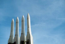 Four white missile launchers pointing upward against a blue sky