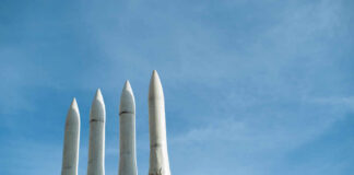Four white missile launchers pointing upward against a blue sky