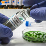 Deadly Germ Lurks In Deli Meat? A laboratory technician holding a vial labeled 'Listeria monocytogenes' above a petri dish with green culture