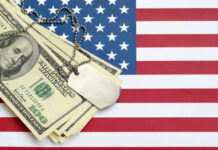 A stack of dollar bills on an American flag with a military dog tag