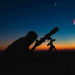 Space Sugar Twist Stuns Scientists Silhouette of person using telescope against colorful twilight sky.