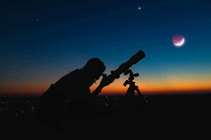 shutterstock_1715179471-1 Silhouette of person using telescope against colorful twilight sky.