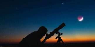 Silhouette of person using telescope against colorful twilight sky.