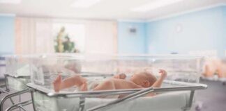 Newborn baby lying in a transparent crib in a hospital nursery