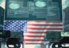 A high-tech workspace featuring multiple computer monitors displaying data and an American flag in the background