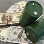 UPDATE: Oil Slide Nears Pre-War Lows Two green barrels placed on a pile of hundred dollar bills