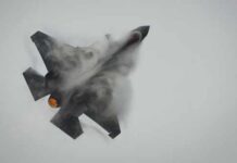 Fighter jet performing an aerial maneuver with smoke trailing behind