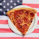Pizza Giant Bleeds Cash, Slams Doors Pepperoni pizza slice on a paper plate over an American flag