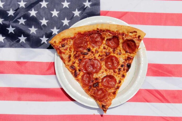 Pizza.,A,Slice,Of,Pepperoni,Pizza,On,An,American,Flag. Pepperoni pizza slice on a paper plate over an American flag