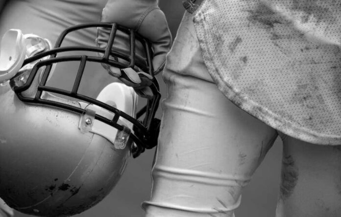 shutterstock_50223526 Football player holding helmet, dirty uniform close-up.