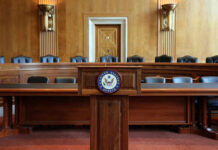 Unlikely Duo Demands Millions — Why Now? Empty Senate chamber with a wooden podium and chairs