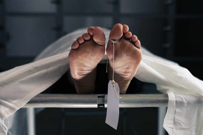 Feet of a covered body on a morgue table with a toe tag