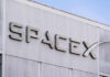 Gravity Targets SpaceX — Lunar Smash Imminent SpaceX building logo against blue sky.