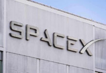 Gravity Targets SpaceX — Lunar Smash Imminent SpaceX building logo against blue sky.