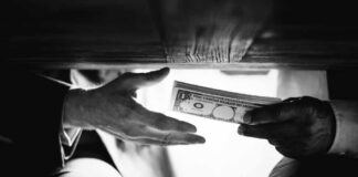 Hands passing money under a table, shrouded in mystery.