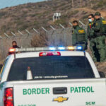 Border Patrol agents and vehicles at fenced border area.