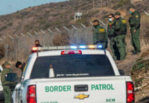 Border Patrol agents and vehicles at fenced border area.
