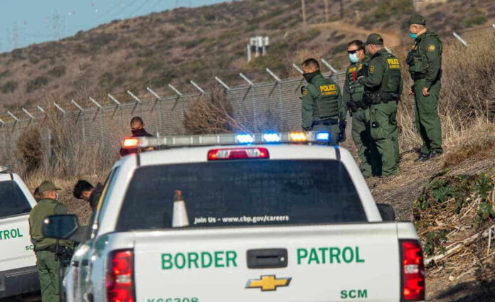 Border Patrol agents and vehicles at fenced border area.