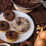Milk Bomb in Donut Aisle Chocolate glazed donuts on a patterned plate with baking ingredients
