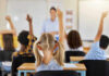 Kids Hooked Daily — Doctors Sound Alarm Children raising hands in classroom, teacher in background.
