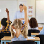Kids Hooked Daily — Doctors Sound Alarm Children raising hands in classroom, teacher in background.