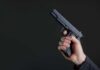 Hand holding a black semi-automatic pistol against a dark background