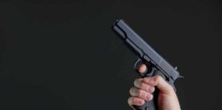 Hand holding a black semi-automatic pistol against a dark background