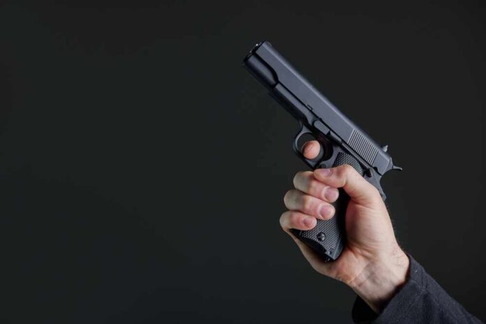 Male,Hand,Holding,A,Gun,On,Black,Background,.,A Hand holding a black semi-automatic pistol against a dark background