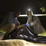 Lake Mead Bones Spark New Mystery forensic team examines a body bag at a nighttime outdoor crime scene