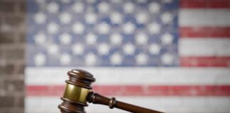 A wooden gavel resting on a sound block with an American flag background