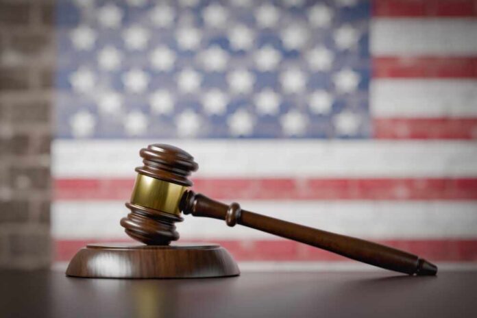 American,Flag,On,Wall,Behind,Gavel,Resting,On,Table. A wooden gavel resting on a sound block with an American flag background
