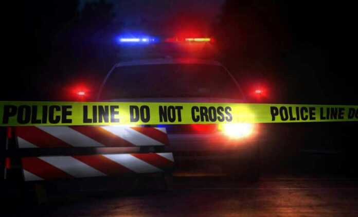 shutterstock_693454099 Police car with flashing lights behind caution tape.