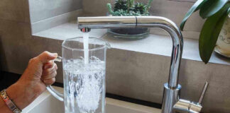 Hand filling pitcher with water from faucet.