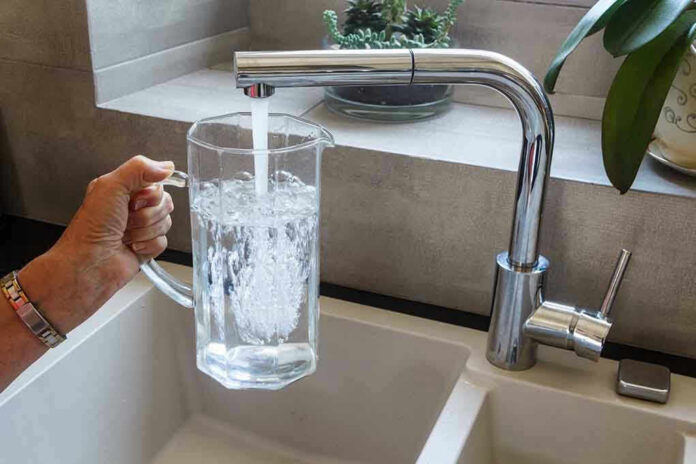 1450697639 Hand filling pitcher with water from faucet.