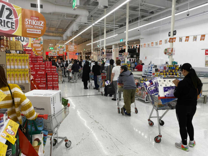 shutterstock_1665087292 Shoppers queue with carts in a supermarket checkout area