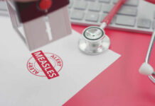 Deadly Measles Hits Blue State Again A stamp marking 'MEASLES ALERT' on a piece of paper next to a stethoscope and keyboard
