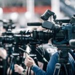 SpaceX vs Amazon: Phone Coverage Clash Broadcast cameras on tripods at a press event
